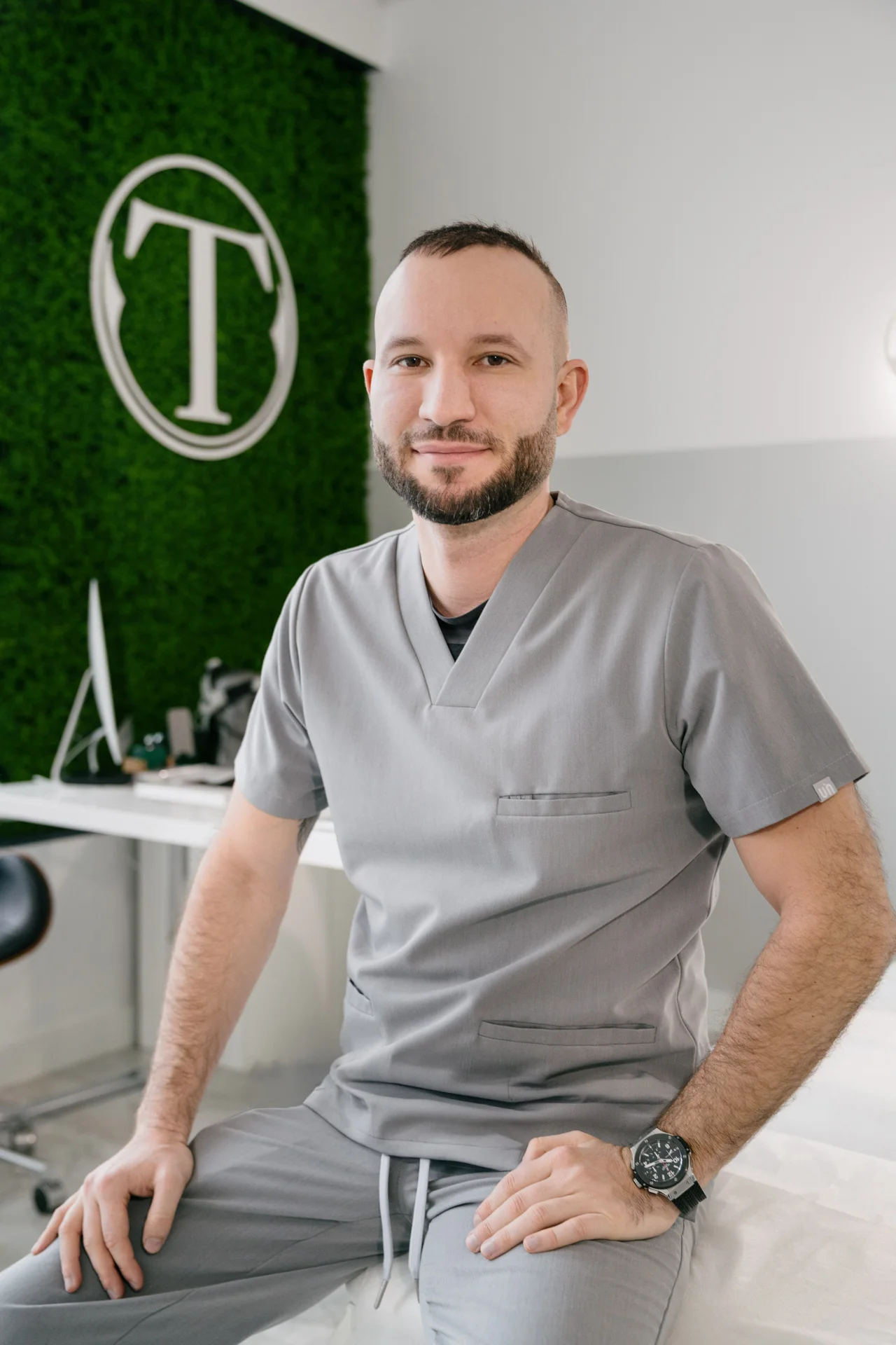 dr Kotapka w szarym stroju medycznym na tle zielonej ściany